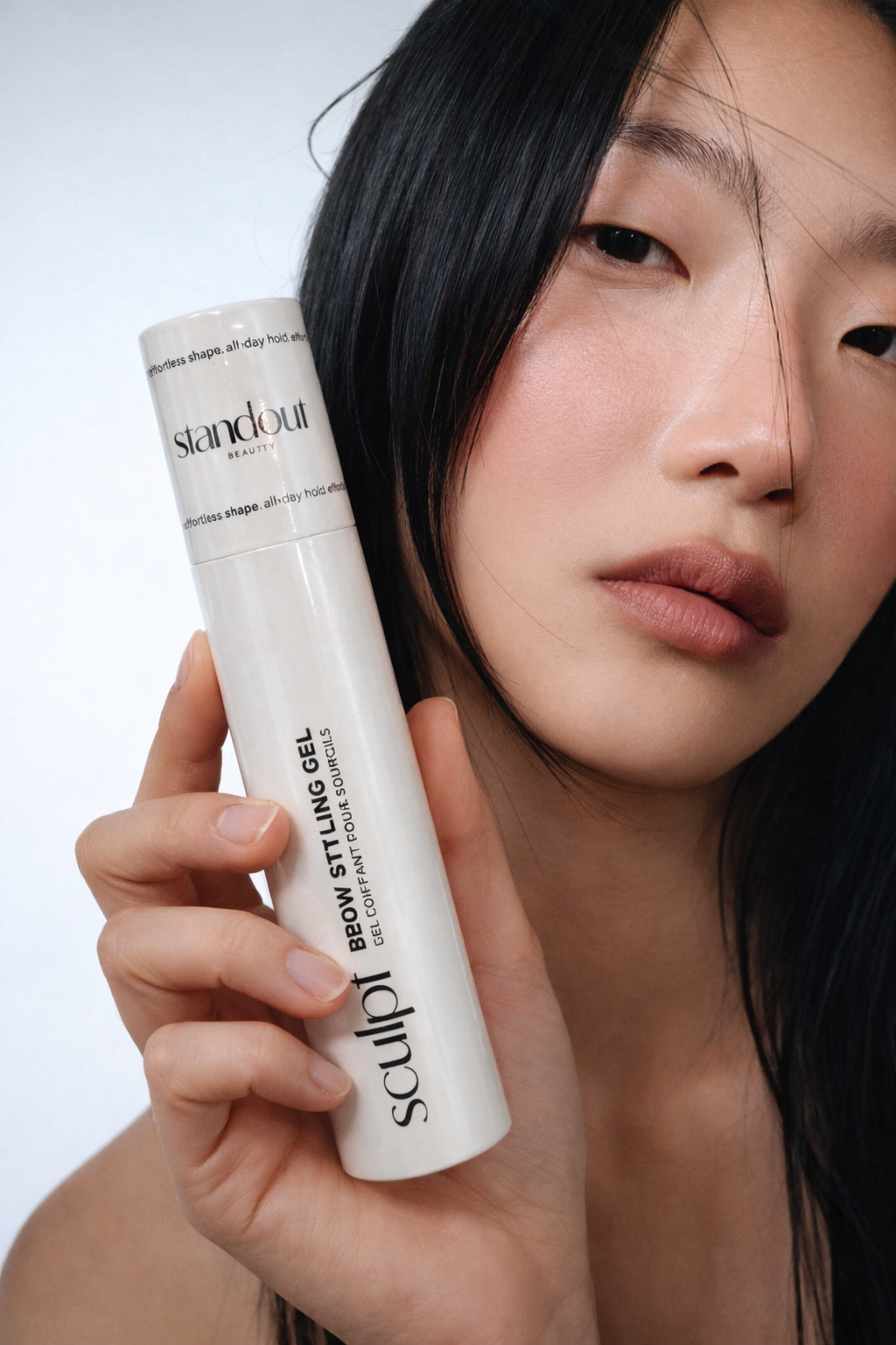 Person holding a bottle of 'Sculpt' brow styling gel with a neutral background